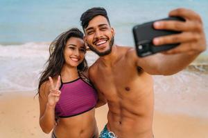 feliz pareja viajera haciendo fondo de playa selfie, colores soleados de verano, estado de ánimo romántico. caras emocionales de risa feliz. foto