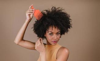 joven mujer latina peinándose. tenedor para peinar el cabello rizado. fondo pastel foto