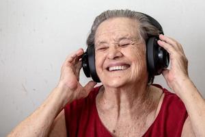 Funny old lady listening music and dancing on white background. Elderly woman wearing glasses dancing to music listening on his headphones. photo