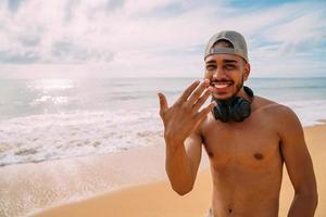 amable joven latinoamericano invitando a venir a brasil, confiado y sonriente haciendo un gesto con la mano, siendo positivo y amigable foto