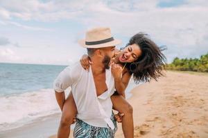 Pareja joven en vacaciones de verano en la playa, feliz hombre sonriente lleva a la mujer de vuelta al mar foto