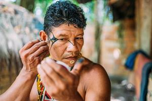 Indian from the Pataxo tribe, using a mirror and doing face painting. photo