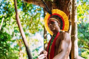 indio de la tribu pataxo usando un arco y una flecha. indio brasileño con tocado de plumas y collar foto