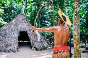 indio de la tribu pataxo usando un arco y una flecha. indio brasileño con tocado de plumas y collar
