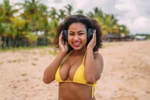 summer holidays, technology and internet concept. latin american woman listening music with headphone and sunning on the beach photo