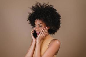 Image of excited young Latin woman surprised using cellphone on pastel background. photo