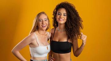 Blonde and brunette women having fun portrait against yellow background. A blonde and a brunette. Different types of hair. Racial diversity. Friends. photo