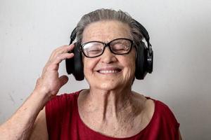 Funny old lady listening music and dancing on white background. Elderly woman wearing glasses dancing to music listening on his headphones. photo