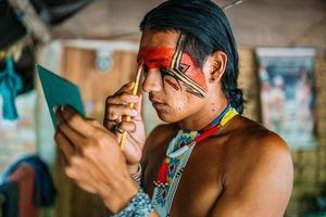 indígena de la tribu pataxo, usando un espejo y pintándose la cara. foto