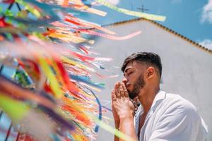 hombre latinoamericano haciendo un pedido con cintas brasileñas en la cerca de una iglesia en arraial d'ajuda, bahia, brasil. centrarse en cintas de colores foto