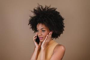 Image of excited young Latin woman surprised using cellphone on pastel background. photo