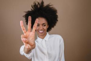 mujer latina sonriente haciendo tres tiempos de cuenta regresiva gesto de signo con los dedos de la mano sobre fondo pastel. foto