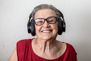 Funny old lady listening music and dancing on white background. Elderly woman wearing glasses dancing to music listening on his headphones. photo