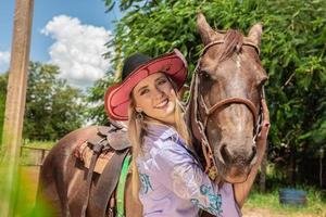 Beautiful blonde cowgirl with hat standing near the horse ranch background photo