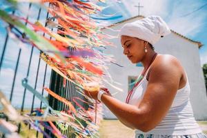 mujer brasileña vestida con el traje tradicional bahiano de la religión umbanda rezando. concéntrese en cintas de colores de promesas religiosas en devoción a senhor do bonfim en bahia, brasil foto