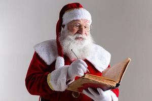 Santa Claus with a old red cover book. Jotting down names gifts for Christmas. Christmas is coming photo