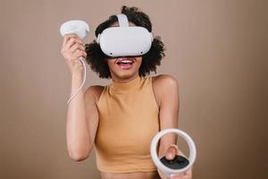 Latin young woman standing with VR goggles and keep joysticks or finger as a gun. photo