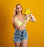 mujer rubia de pelo largo con una pandereta de juguete en las manos. sobre fondo amarillo. chica brasileña. carnaval. río foto
