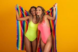 amigas mujeres disfrazadas disfrutando de la fiesta de carnaval cubriendo con la bandera del orgullo lgbt foto