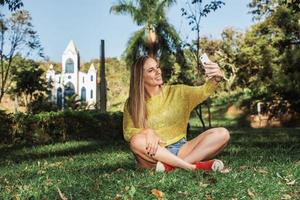 hermosa mujer tomando selfie con su teléfono inteligente en el campo. iglesia en segundo plano. foto