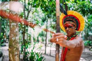 indio de la tribu pataxo usando un arco y una flecha. indio brasileño con tocado de plumas y collar foto