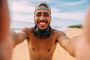 Amable sonriente joven latinoamericano. hombre con gorra y auriculares, sosteniendo y mirando a la cámara foto