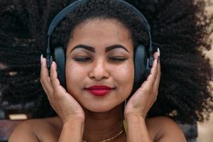 summer holidays, technology and internet concept. latin american woman listening music with headphone and sunning on the beach photo