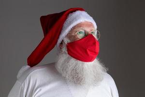 Santa Claus smiles behind red Covid-19 safety face mask. Christmas with social distance. photo