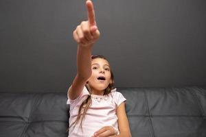 Happy little girl watching tv in the night sitting on a couch in the living room at home photo