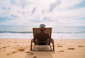 vacaciones de verano, tecnología y concepto de internet. hombre latinoamericano sentado en la silla de playa, escuchando música con auriculares y tomando el sol en la playa foto