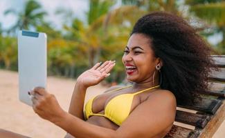 Man making a video call on summer vacation. latin american man sitting on the beach chair with headphones and a tablet photo