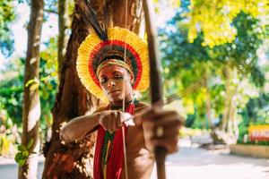 indio de la tribu pataxo usando un arco y una flecha. indio brasileño con tocado de plumas y collar. centrarse en indio foto