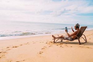 Man making a video call on summer vacation. latin american man sitting on the beach chair with headphones and a tablet photo