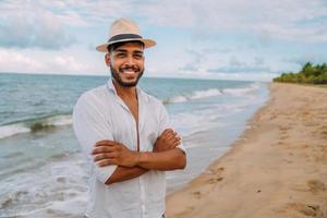 amistoso, joven, latinoamericano, hombre, con, armamentos cruzaron, en la playa, llevando, un, sombrero foto