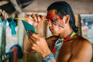 indígena de la tribu pataxo, usando un espejo y pintándose la cara. foto