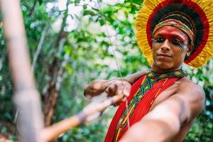 indio de la tribu pataxo usando un arco y una flecha. indio brasileño con tocado de plumas y collar