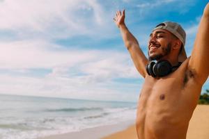 vacaciones de verano, tecnología y concepto de internet. hombre latinoamericano sonriente y feliz con los brazos abiertos. hombre con auriculares y gorra foto