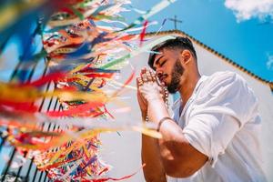 hombre latinoamericano haciendo un pedido con cintas brasileñas en la cerca de una iglesia en arraial d'ajuda, bahia, brasil. centrarse en cintas de colores foto