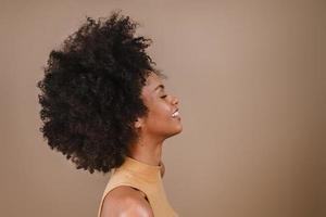 Side a smiling young Latin afro woman. Joy, positive and love. Beautiful african-style hair. Pastel studio background. photo