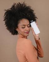 Beauty Latin woman with afro hairstyle. Brazilian woman. Holding blank shampoo packaging. Curly hair. Hair style. Pastel background. photo