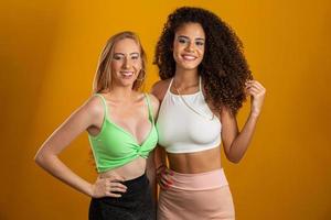 Blonde and brunette women having fun portrait against yellow background. A blonde and a brunette. Different types of hair. Racial diversity. Friends. photo