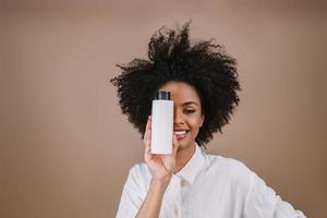 Beauty Latin woman with afro hairstyle. Brazilian woman. Holding blank shampoo packaging. Curly hair. Hair style. Pastel background. photo