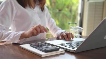 zakenvrouw handen werken met financiën over kosten en rekenmachine en laptop met tablet, smartphone op kantoor in ochtendlicht video