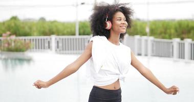 African woman in sportswear wearing headphones dancing at swimming pool background . video