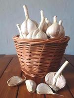 Closeup garlic are in the wicker basket on the wooden table photo