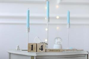 concepto de día de san valentín. calendario de cubo de madera con fecha del 14 de febrero con corazón de madera blanca desde arriba sobre la mesa. candelabros blancos con fondo de velas azules y bokeh con luz foto