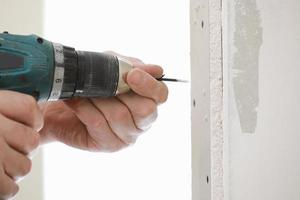 The installer worker in safe medical mask and overalls fixes a detail of the stiffener element with screws using an electric screwdriver to the wall of the metal structure photo