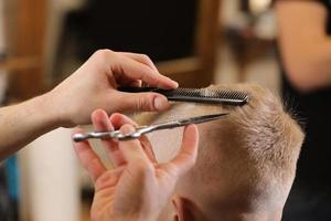 peluquería masculina, corte de pelo, en una barbería o peluquería. primer plano de las manos del hombre acicalando el cabello del niño en la peluquería. retrato de niño varón en la peluquería para cortarse el pelo. foto