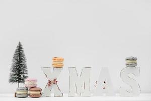 The wooden word xmas with colorful macaroons or macarons and christmas tree on white background. Xmas decoration. New Year home decor photo