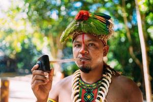 jefe indio de la tribu pataxo fumando pipa. indio brasileño con tocado de plumas y collar mirando a la cámara foto
